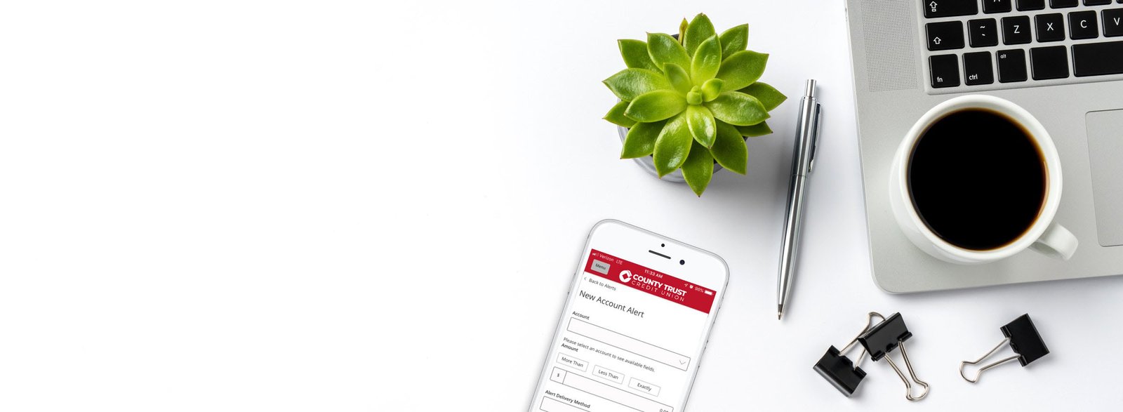 Phone with Crawfield Credit Union app alerts screen, laptop on tabletop